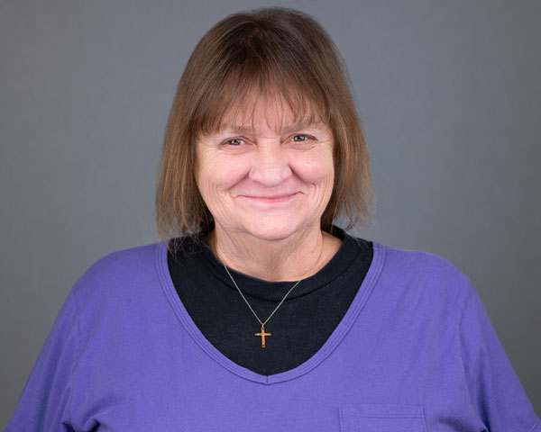 A woman with brown hair wearing a purple shirt.