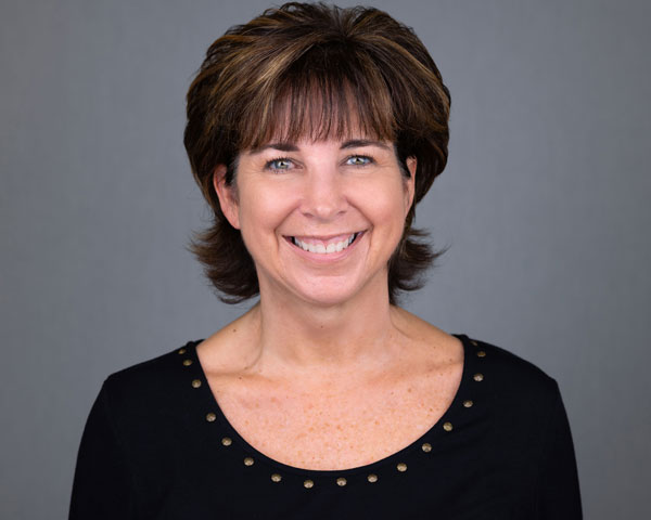 A woman with brown hair and black shirt smiling.