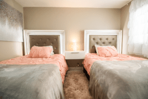 Two beds in a bedroom with pink and grey bedding.