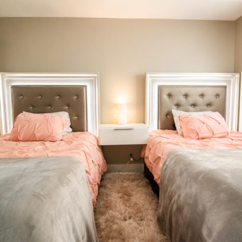 Two beds in a bedroom with pink and grey bedding.
