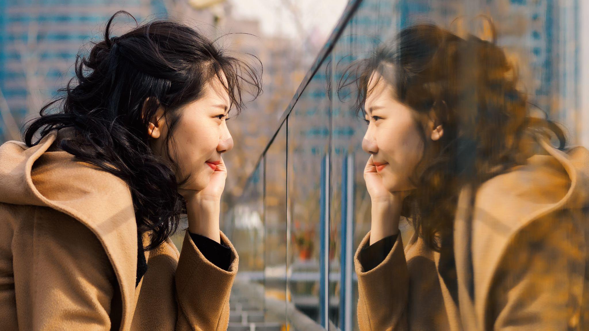 A woman is looking at her reflection in the mirror.