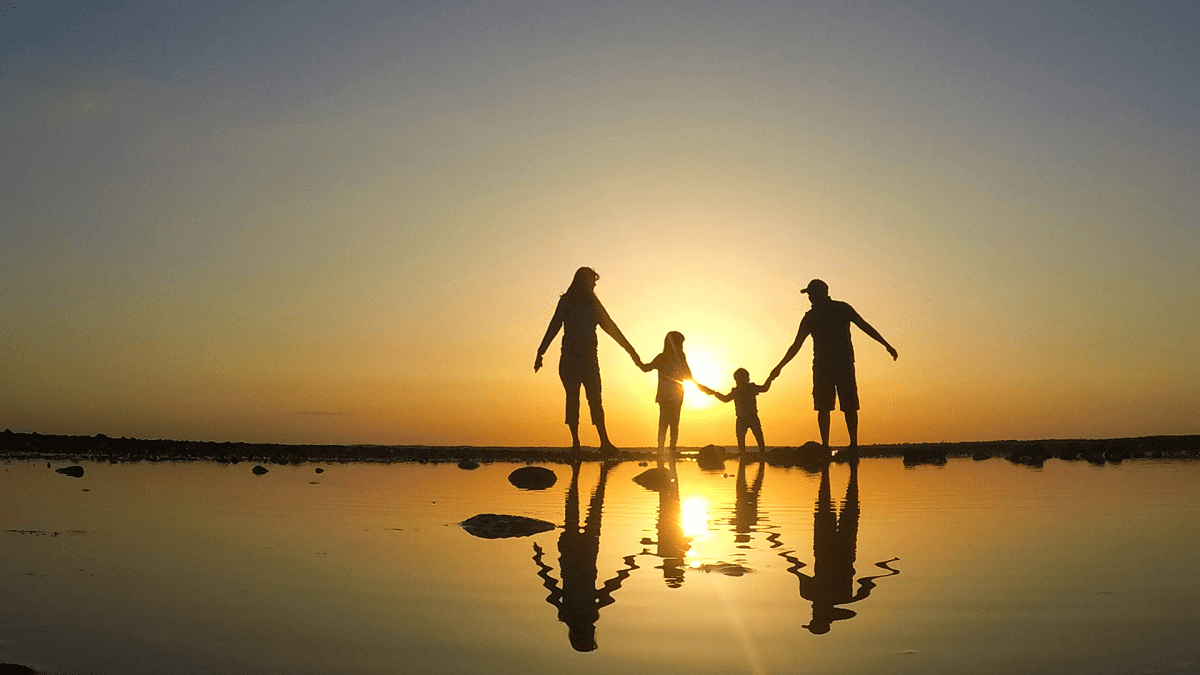 A family is holding hands at sunset on the beach.