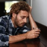 A man sitting on the edge of a bench looking at his phone.
